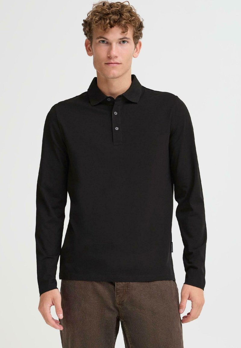 Čierna polokošeľa s dlhým rukávom a golierom, tromi gombíkmi a textúrovaným povrchom, v kombinácii s hnedými nohavicami.