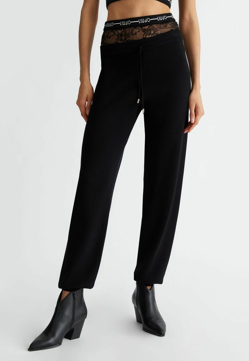 Czarne spodnie dresowe z koronkowym pasem w talii, wyposażone w sznurki i dopasowany krój. Połączone z czarnymi, spiczastymi botkami za kostkę.