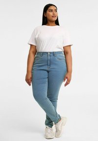 Vaaleansiniset korkeavyötäröiset farkut, joissa on sileä pinta, viiden taskun muotoilu ja hienovaraiset ompeluyksityiskohdat, yhdistettynä yksinkertaiseen valkoiseen paitaan ja tennareihin.