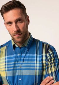 Camicia a maniche corte con un motivo a quadri multicolore che presenta tonalità di blu e verde. Tessuto di cotone, colletto con bottoni.