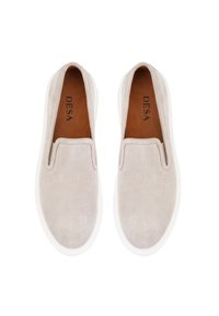 Beige suede instappers met witte rubberen zolen, een gladde textuur en minimale stiksels, met een bruine binnenvoering en merktekst.