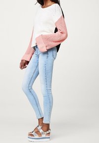 Neulottu pusero, jossa valkoisia, vaaleanpunaisia ja mustia värilohkoja; väljät hihat. Vaaleansiniset kapealahkeiset farkut ja hopeiset korolliset sandaalit remmeillä.