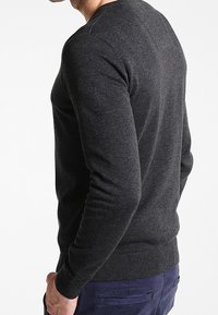 Pull en maille gris avec des manches longues, un décolleté arrondi et un ourlet côtelé. Le matériau semble doux avec une finition texturée.