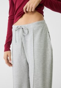 Lys grå svedebukser med snore i taljen, sidelommer og et blødt, struktureret materiale. Delvist synlig bordeaux langærmet bluse.