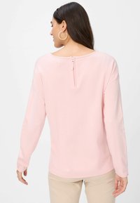 Lichtroze lange mouw top met een ronde halslijn en een ritsdetail aan de achterkant. Zachte stof met een gladde textuur, in combinatie met beige broek.