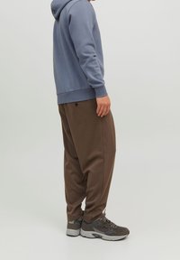 Bluza z kapturem w jasnoniebieskim kolorze z ściągaczami, zestawiona z luźnymi brązowymi spodniami dresowymi z kieszenią i elastycznym paskiem. Szare sneakersy.