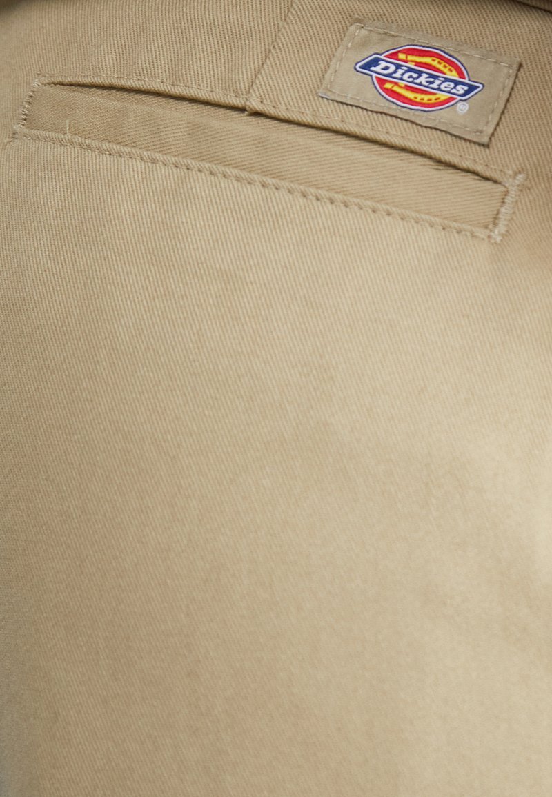 Beige, strukturiertem Stoff mit einer Tasche auf der Rückseite und einem genähten Dickies-Logoetikett. Das Material wirkt robust und langlebig.