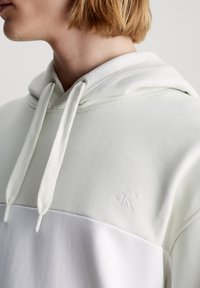Sudadera con capucha en verde claro y blanco. Tela suave con acentos texturizados, con un pequeño logo bordado en el pecho.