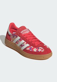 Zapatilla Adidas roja con rayas blancas, suela de goma, patrón floral en las secciones de tela, texto "Spezial" y superposiciones de ante rojo.