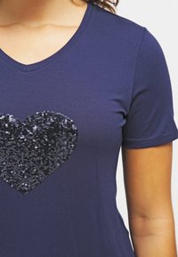 Navy blue t-shirt in soft fabric with short sleeves, featuring a large black sequin heart design on the front. V-neckline.