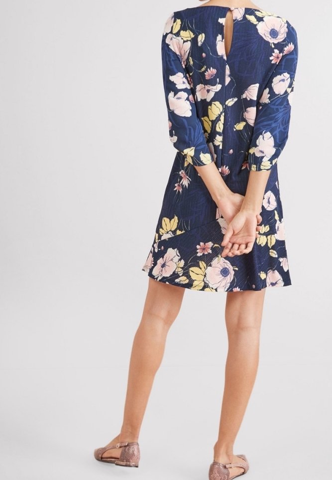 Robe fleurie bleu marine à manches trois-quarts, avec un détail dos à découpes en forme de goutte et un ourlet évasé, associée à des chaussures plates marron clair.