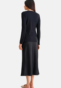 Haut à manches longues noir côtelé associé à une jupe midi en satin noir fluide. Texture lisse et design ajusté, avec un style minimaliste.