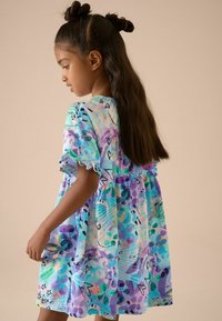 Kurzärmliges, knielanges Kleid in Pastellblau mit mehrfarbigen abstrakten Mustern. Weicher Stoff mit gerafften Ärmelenden und elastischem Bund.