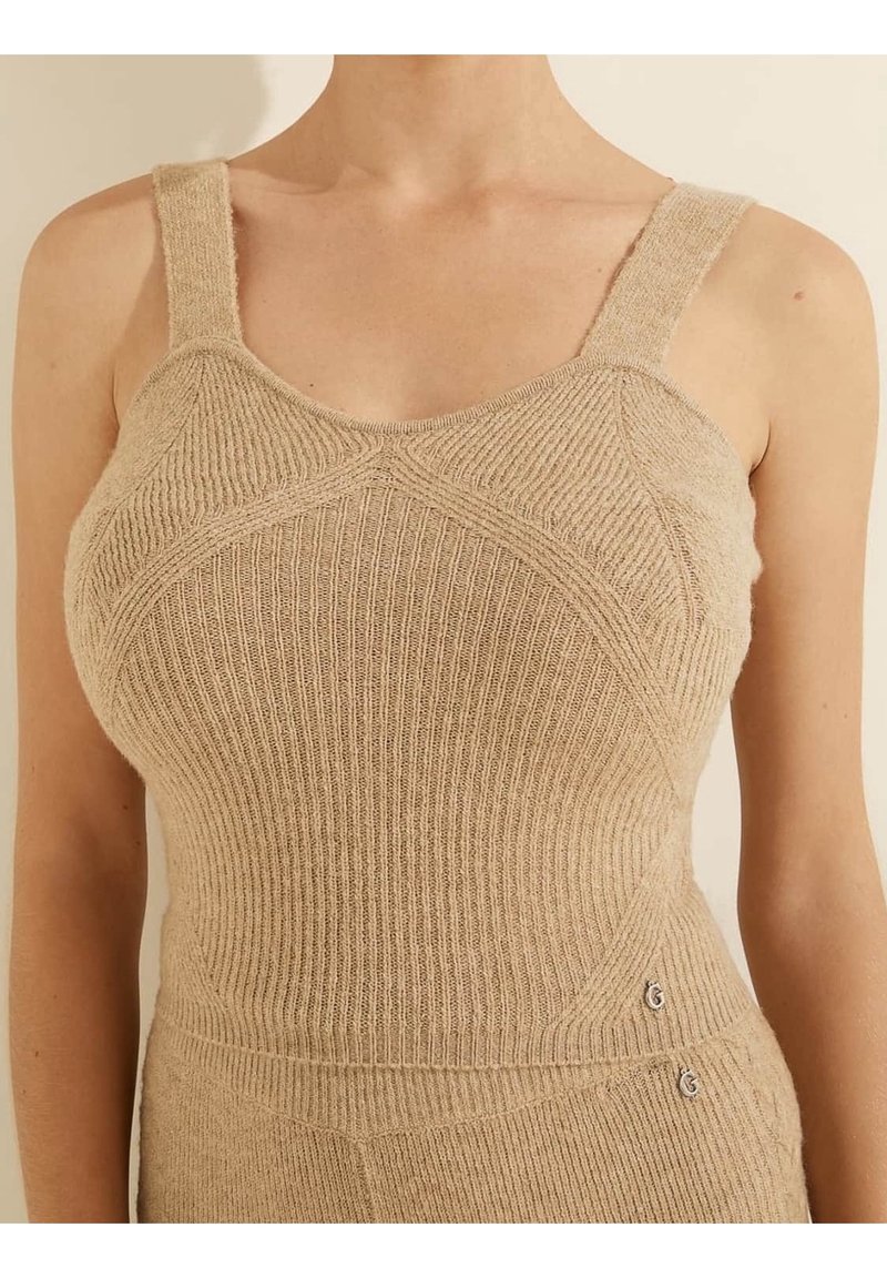 Gros plan d'une personne portant un haut sans manches beige en maille côtelée avec de larges bretelles et des motifs en maille texturée.