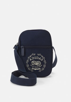 Small navy blue Adidas shoulder bag with front zipper pocket and adjustable strap, featuring a white logo and decorative text on front.