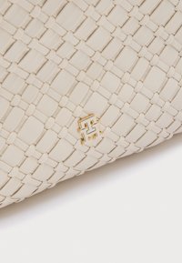 Sac à main en cuir tressé beige avec un accent logo doré. La texture est lisse avec un design structuré et des détails de motif entrelacé.