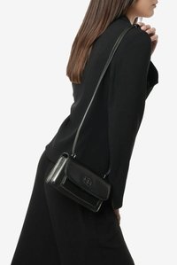 Czarna skórzana torebka na ramię z klapką i tłoczonym logo, posiadająca cienki pasek i błyszczącą fakturę. Kompaktowy prostokątny kształt.