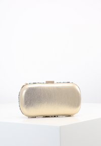 Clutch metálico dorado con superficie texturizada, forma redondeada, adornos florales en azul y rosa, y cierre tipo clasp en la parte superior.
