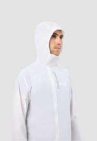 Biała lekka kurtka przeciwdeszczowa z kapturem, zapinana na zamek błyskawiczny z przodu, z refleksyjnymi detalami logo. Gładka faktura i oddychający design.