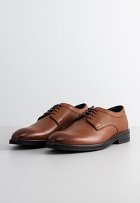 Braune Leder-Schnürschuhe mit glatter Textur und perforierten Details an den Seiten. Flache Gummisohle und klassisches Design.