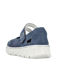 Chaussure en daim bleu avec lanière ajustable, côtés ouverts et semelle épaisse blanche présentant un motif texturé. Logo de la marque embossé sur le côté extérieur.