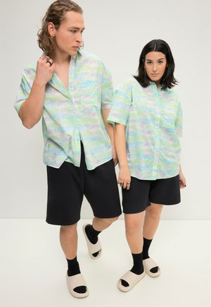 Kortærmede, lysegrønne skjorter med knap, prydet med abstrakte mønstre, parret med sorte shorts og beige slip-on sandaler. Glat tekstur.