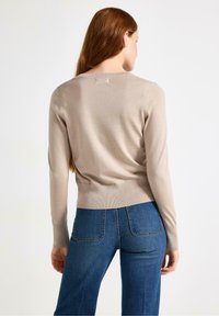 Maglione beige a maniche lunghe con polsini e orlo a coste, caratterizzato da un collo rotondo. Abbinato a jeans in denim blu, con una vestibilità classica.