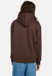 Bruine hoodie met een capuchon, gemaakt van zacht materiaal; heeft een geribbelde zoom en manchetten, gecombineerd met lichtblauwe denim broek.