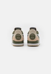 Sneakers featuring a green and beige color scheme, textured tan accents, a circular logo on the heel, and a lace-up design.