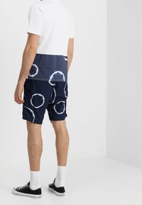 Námořnická bavlněná košile s bílým dip-dye designem. K ní ladící šortky s velkými kruhovými vzory ve světlejších odstínech. Oblečeno s černými teniskami.