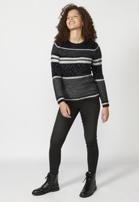Sötétkék alapszínű, szürke és fehér csíkos, valamint gyémántmintás kötött pulóver; fekete skinny farmernadrággal és fűzős csizmával párosítva.