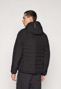 Svart dunjakke med horisontal quilting, tilpasset hette og elastiske mansjetter. Laget av glatt, lett materiale for varme og komfort.