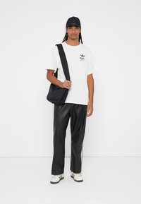 White cotton T-shirt with a small black logo, black shoulder bag, black leather pants, and white sneakers with black accents.