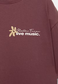 Bordeaux sweatshirt med rund halsudskæring, med et guldblomsterlogo og hvid tekst, der siger "Mellow Tuners live music." Blød tekstur.