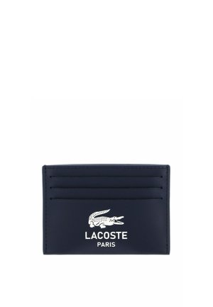 Black cardholder with four card slots and white Lacoste crocodile logo above "LACOSTE PARIS" text on the front.