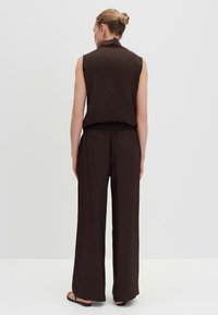 Sleeveless brown top with a high collar paired with loose, wide-leg brown pants, featuring an elastic waistband and a smooth texture.