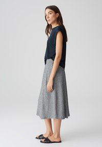 Navyblaues Kurzarmhemd kombiniert mit einem grauen, strukturierten Midilänge-Rock und schwarzen flachen Sandalen. Einfaches, fließendes Design aus weichem Stoff.