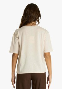 T-shirt a maniche corte color crema con vestibilità rilassata, scollo rotondo, tessuto morbido e senza motivi o loghi visibili, mostrata da dietro.