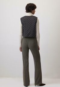 Prugasti crno-bijeli prsluk s visokim ovratnikom, nosi se preko kremaste veste. Maslinasto zeleni široki hlače s detaljem džepa.