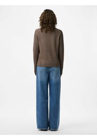 Brun ribbad stickad tröja med långa ärmar, kombinerad med vida blå denimjeans, sedd bakifrån.