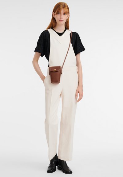Cream-colored jumpsuit with a V-neck design, wide legs, and belt, paired with a black textured top and a brown crossbody bag. Black ankle boots.