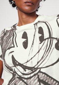 Hvid t-shirt med et stort, sort grafisk design af en tegneseriefigur ansigt, med en rund form og korte ærmer, lavet af blød bomuld.