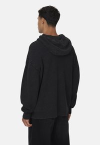 Hoodie nero in maglia con texture a coste, di vestibilità ampia e maniche oversized. Presenta un grande cappuccio e dettagli di design sottili alle cuciture.