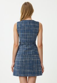 Abito senza maniche blu navy con motivo a quadretti, caratterizzato da una vita aderente e gonna a campana. Il tessuto ha una finitura testurizzata con accenti bianchi.