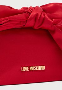 Κόκκινο σατέν τσαντάκι χειρός με λεπτομέρεια κόμπου και χρυσό λογότυπο "LOVE MOSCHINO". Η λεία υφή και το δομημένο σχήμα αναδεικνύουν το σχέδιό του.