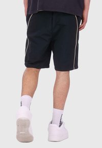Shorts noirs à coupe ample, avec des accents beiges sur les côtés et des ourlets roulés. Portés avec des baskets blanches et des chaussettes montantes.