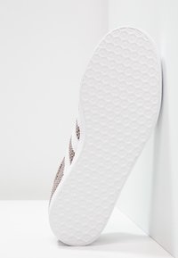 Stickad sneaker i beige och vitt med texturerad yta, med en flexibel, vit gummisula med ett bikakemönster för bra grepp.