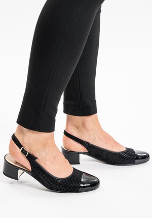 Scarpe slingback nere con tacco basso, lati testurizzati e punte lucide, indossate con pantaloni neri aderenti.
