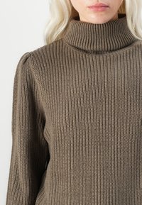 Brun randig polotröja med långa ärmar och subtila axeldetaljer. Tillverkad av strukturerat stickat material som erbjuder värme och komfort.