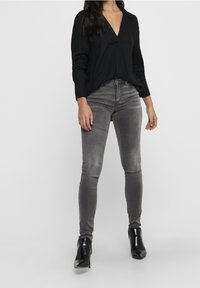 Camisa negra de manga larga con escote en V, combinada con jeans ajustados grises con una textura desgastada y botas de tacón alto negras hasta el tobillo.